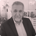 Professional man in a blazer, seated in a modern office setting, with plants and a workspace in the background, representing expertise in SEO services at Olibro Design.